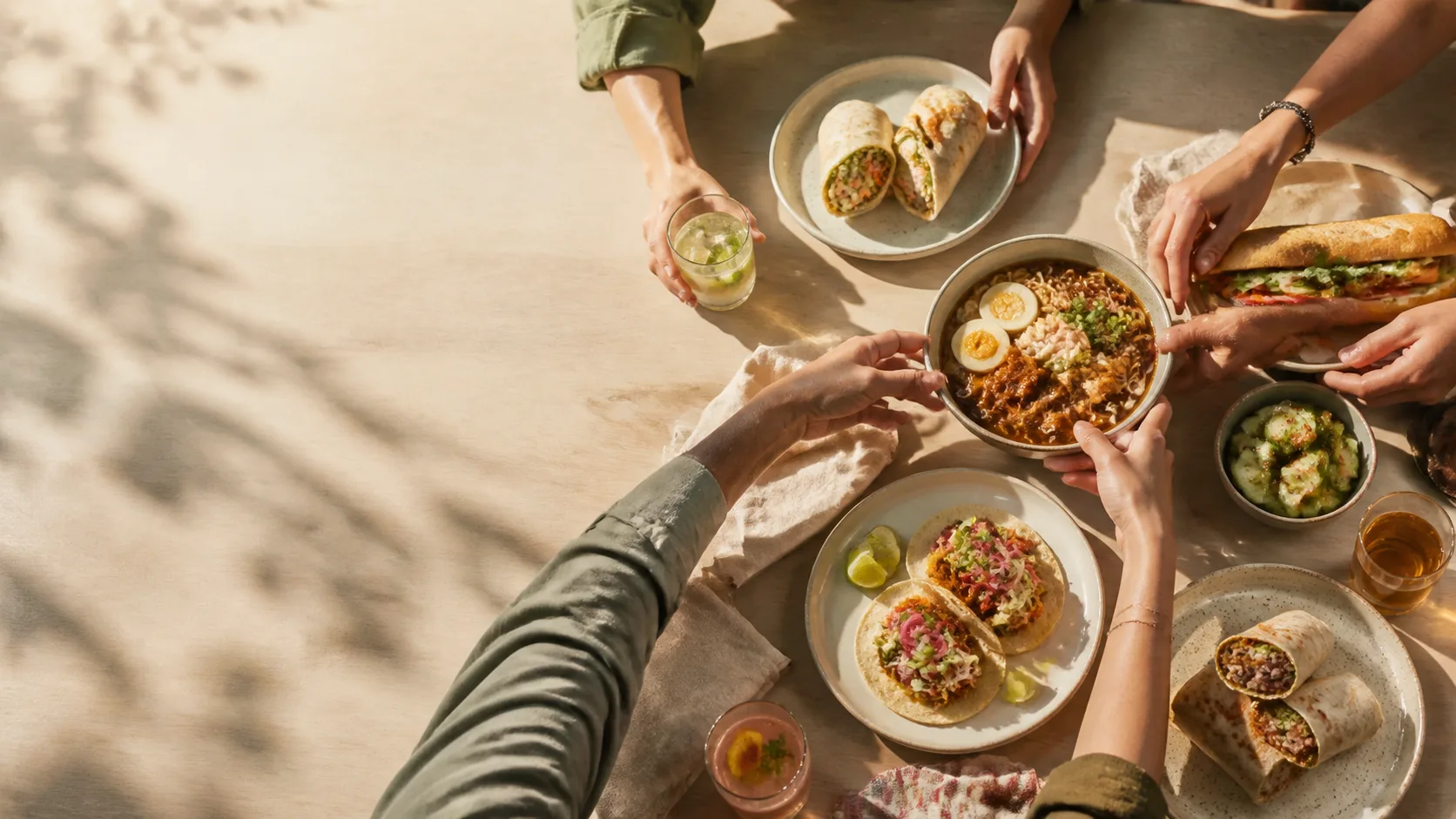 Friends sharing burritos, ramen, tacos, and banh mi around a table